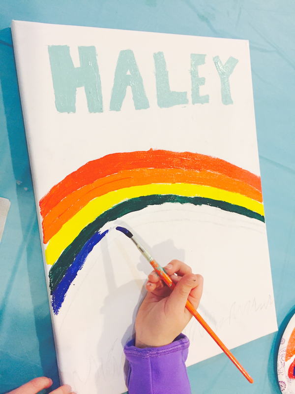 childs hand painting a picture of a rainbow and her name HALEY